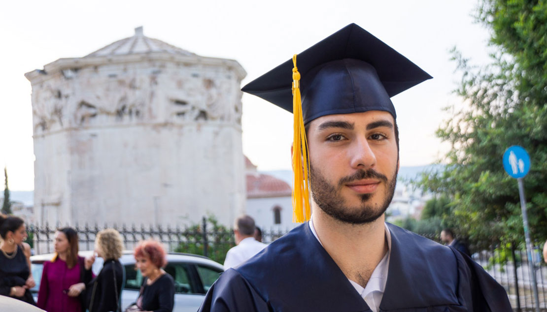 A student graduating from Webster Athens in front of historical building. 
