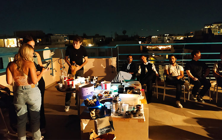 Webster Athens students socialize on the rooftop during the event around a table of food at night..