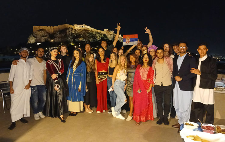 Event attendees from Webster Athens pose on the rooftop for a group photo during the evening event. Some of them are wearing or posing with cultural customs.